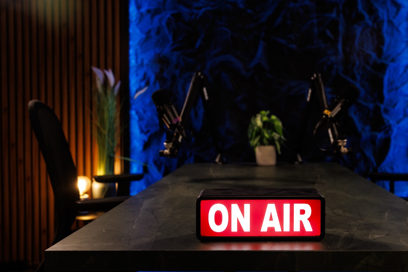 שלט ON AIR דולק על שולחן האבן, עם זרועות המיקרופונים והרקע הכחול מאחור